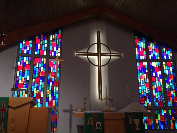 Photo of the front of the sanctuary, with the illuminated cross, pulpit, and covered elements of Holy Communion upon the altar